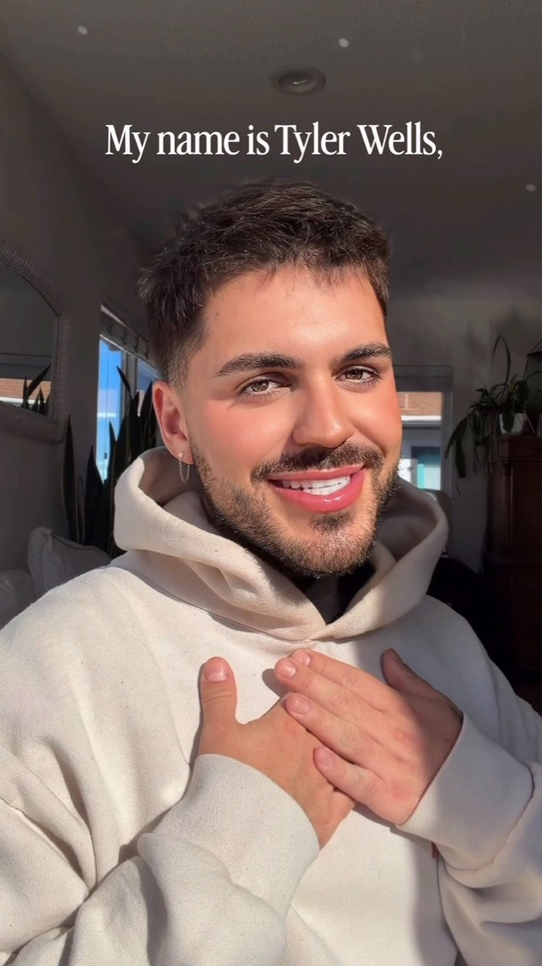 tyler wells in a cream hoodie, hand on his heart, smiling in warm afternoon light